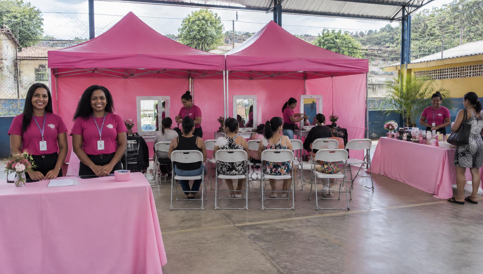 Pátio coberto com duas tendas rosa, recepção, cadeiras organizadas, espelhos e mesa de produtos